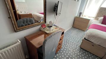 Habitación de hotel con un escritorio de madera, un espejo grande, una cama con ropa de cama blanca y rosa, un radiador y una alfombra estampada.
