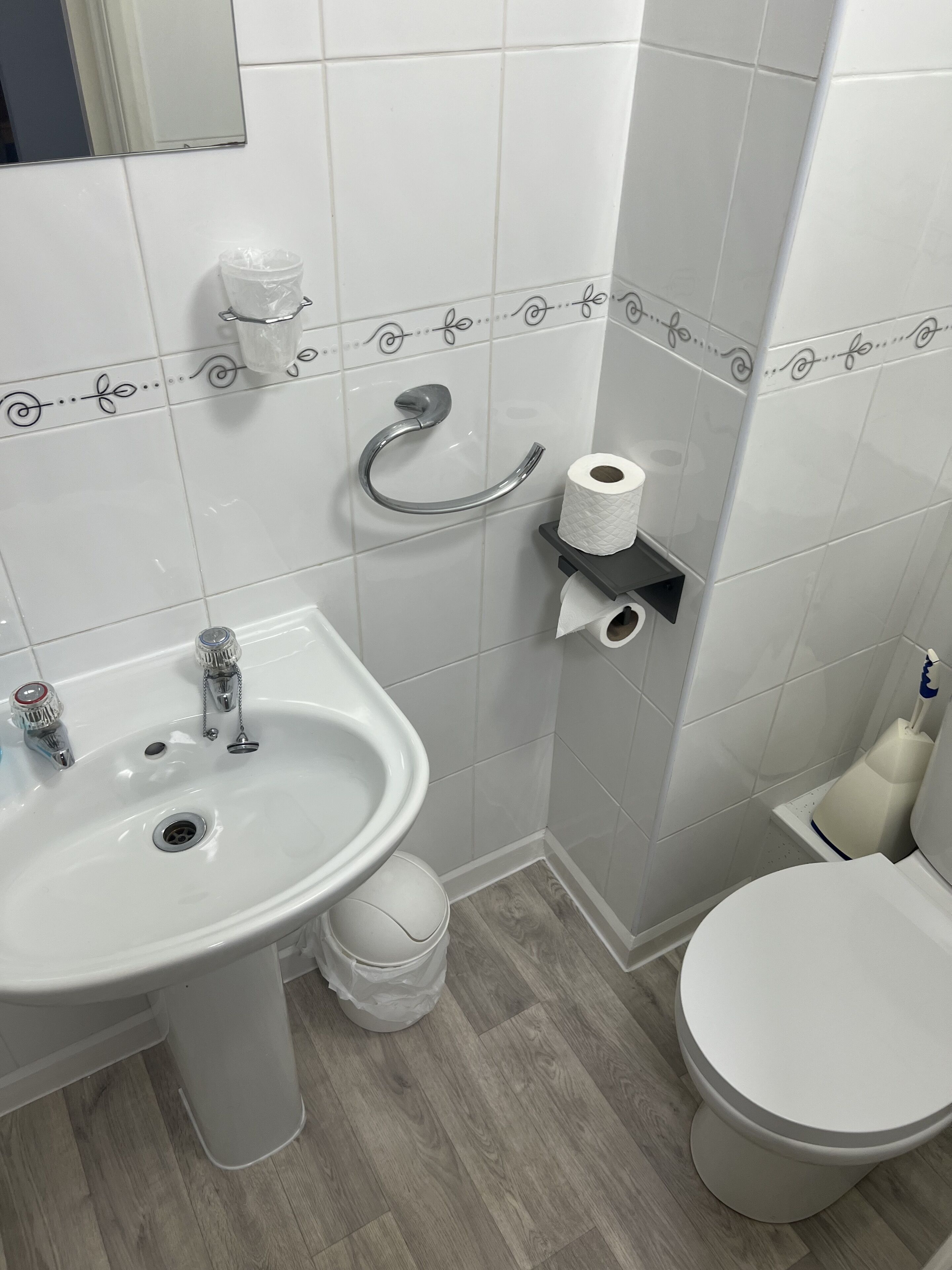 A bathroom with a white sink, toilet, and bidet. There is a toilet paper holder and a hand dryer on the wall.