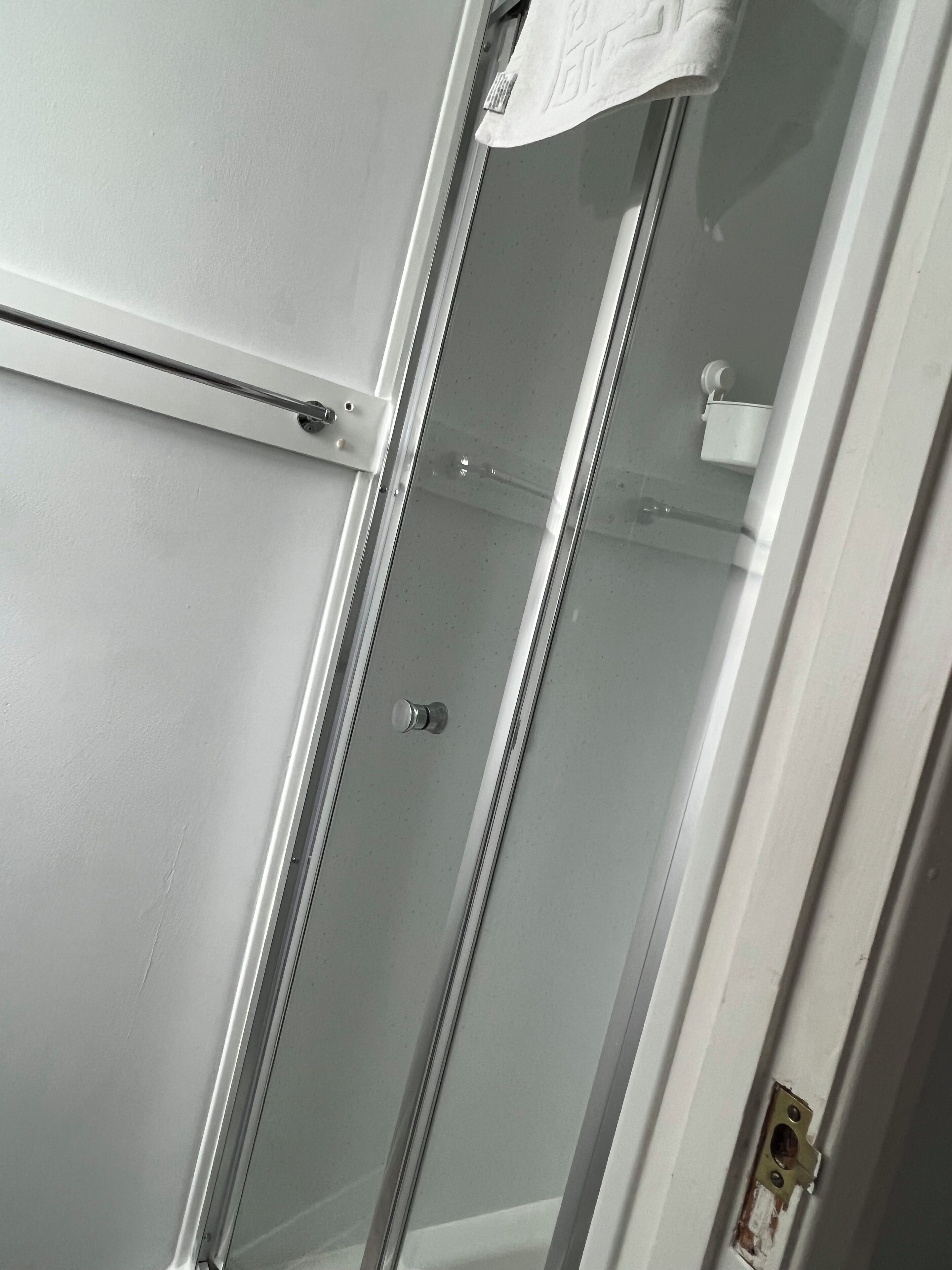 Un baño con cabina de ducha de vidrio, una toalla colgada en la pared y un dispensador de papel higiénico a la vista.