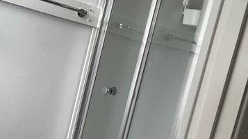 Un baño con cabina de ducha de vidrio, una toalla colgada en la pared y un dispensador de papel higiénico a la vista.