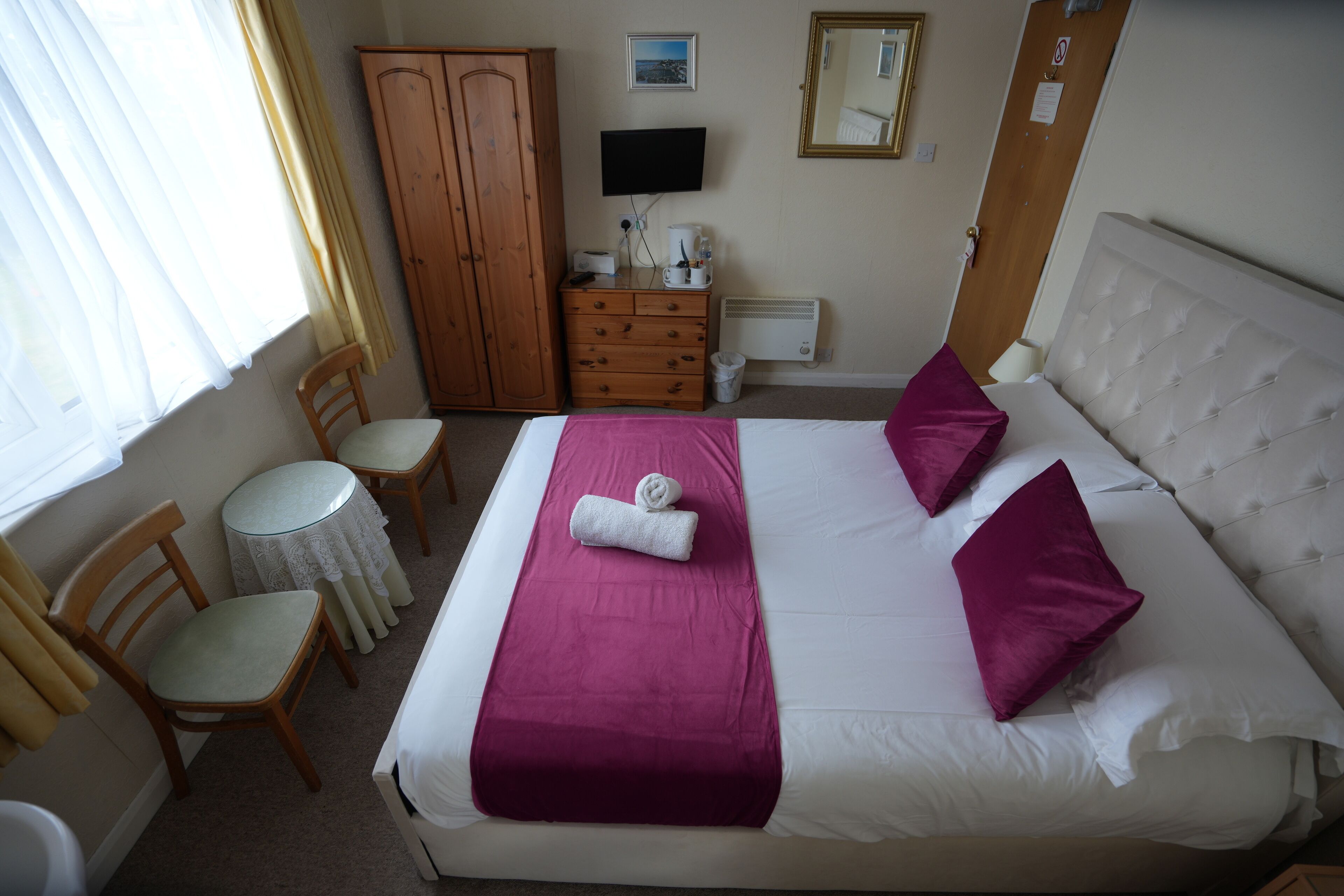 Ein ordentlich eingerichtetes Hotelzimmer mit Bett, Schreibtisch, Stuhl, Kleiderschrank, Fernseher und Spiegel.
