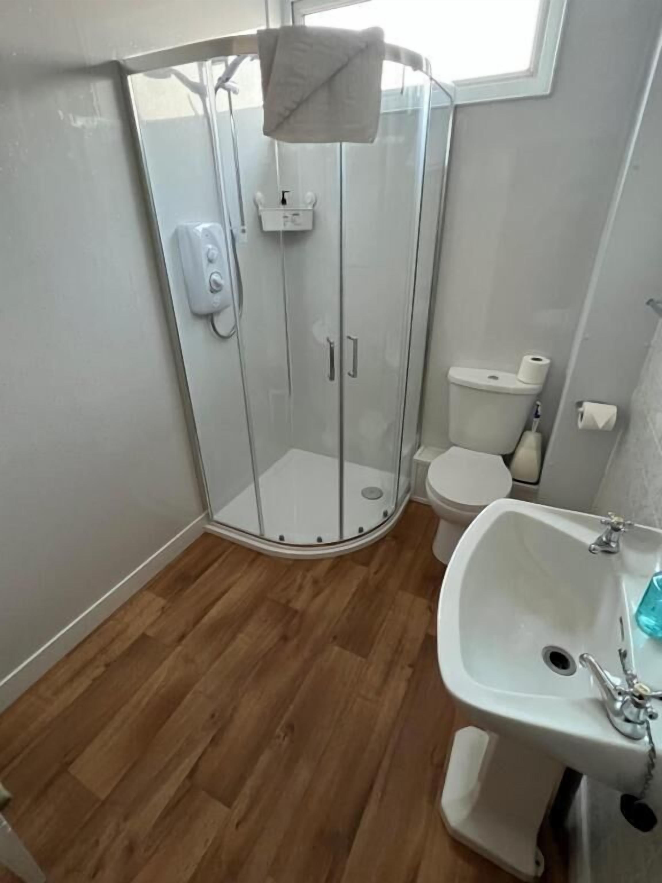 A corner bathroom with a glass shower enclosure, a toilet, and a sink with a mirror.