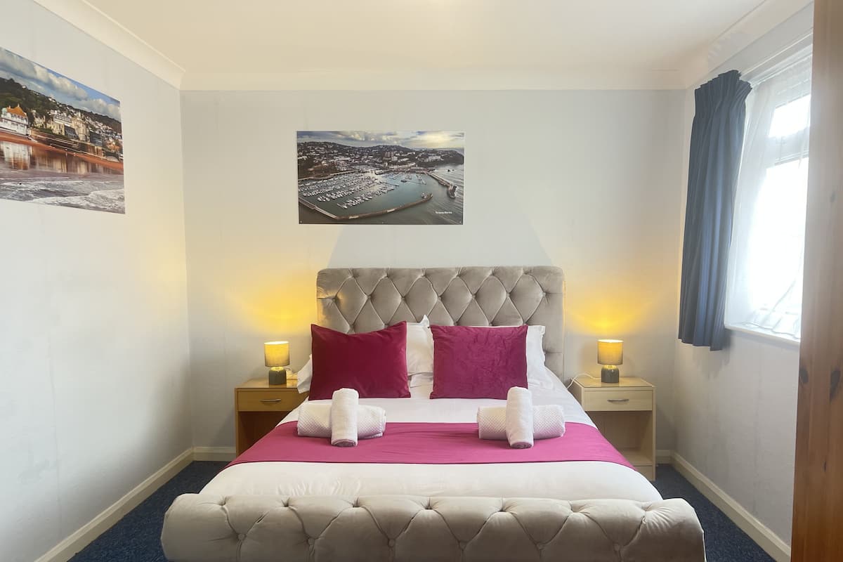 A neatly made bed with a tufted headboard, two bedside lamps, and a framed picture above it.