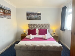 A neatly made bed with a tufted headboard, two bedside lamps, and a framed picture above it. - The Berry Hotel (Paignton)