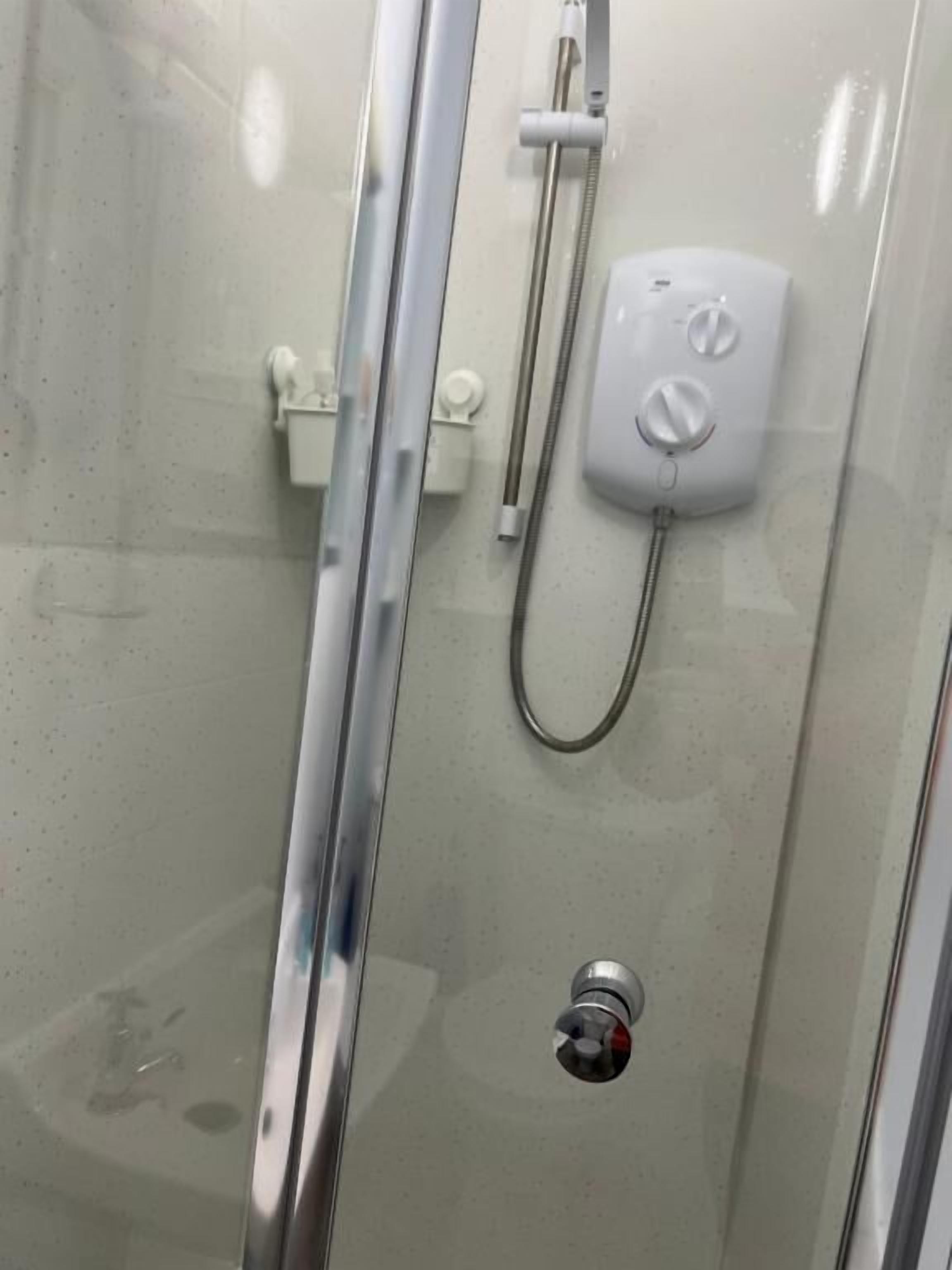 A glass-enclosed shower with a handheld showerhead and a wall-mounted control panel.