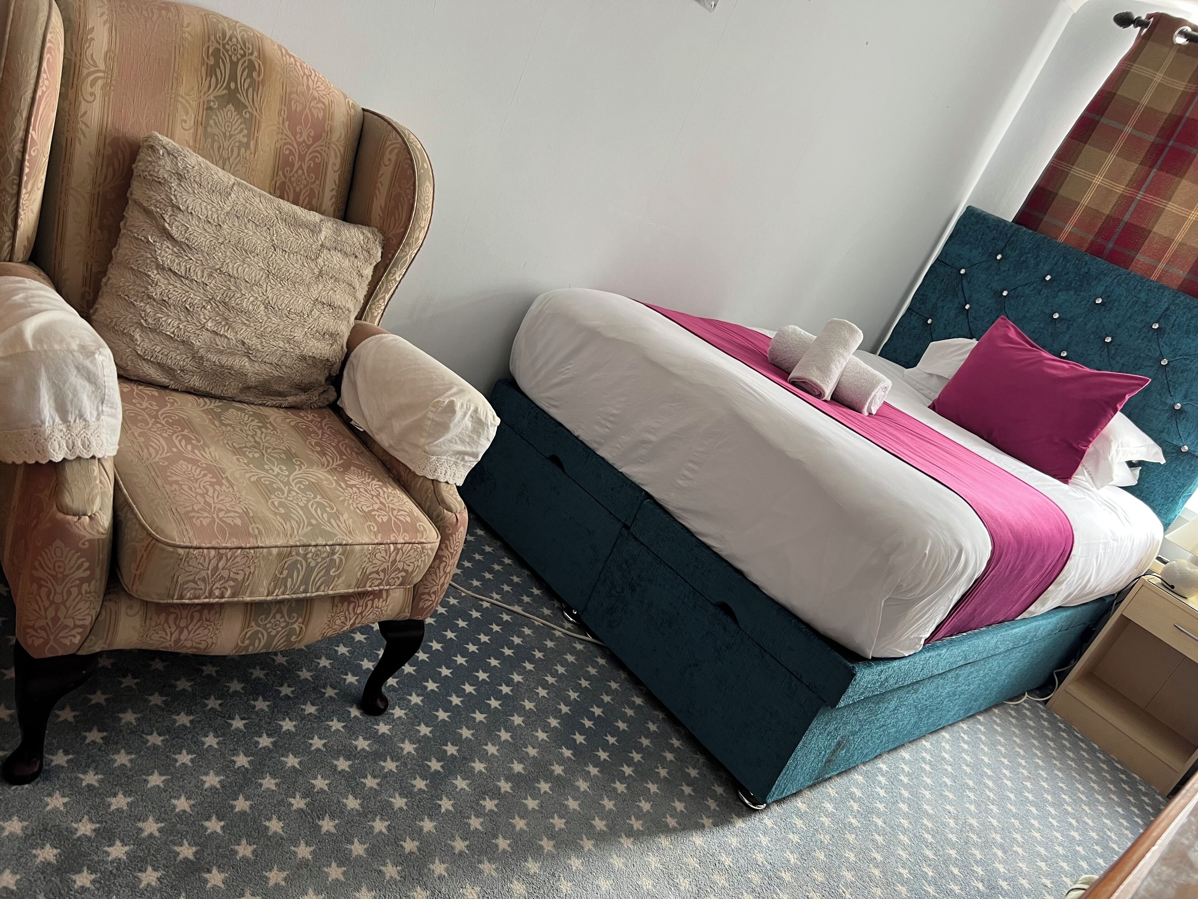 A bedroom with a bed, a chair, and a patterned carpet.