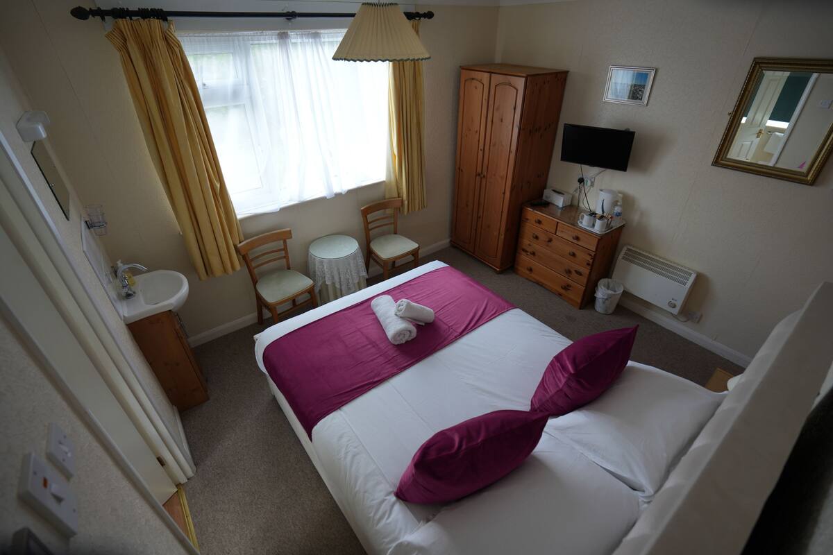 A hotel room with a bed, a desk, a chair, a wardrobe, a mirror, and a window with curtains.