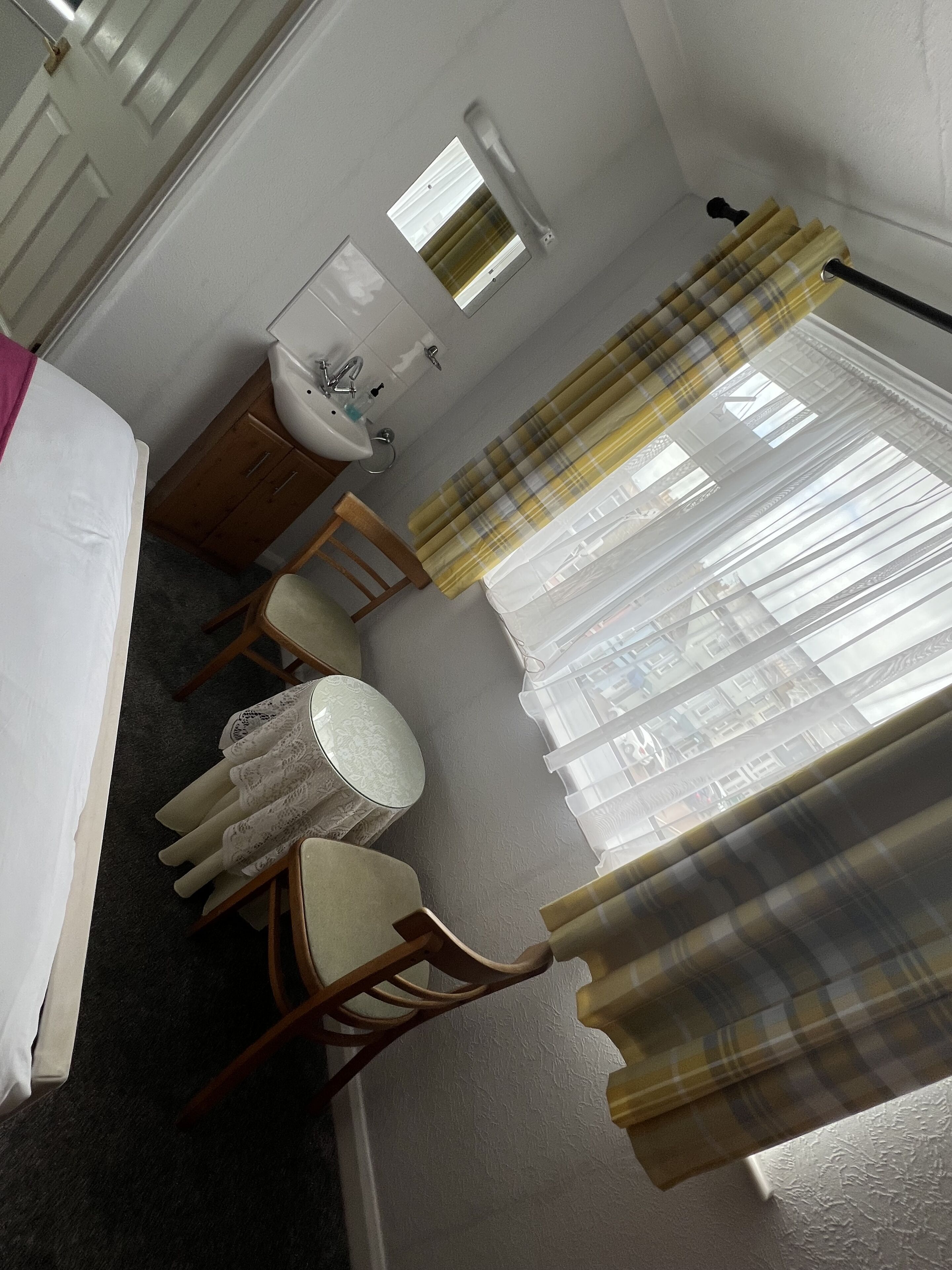 Habitación de hotel con cama, un pequeño escritorio con silla, una mesa redonda con silla, lavabo y ventana con cortinas.