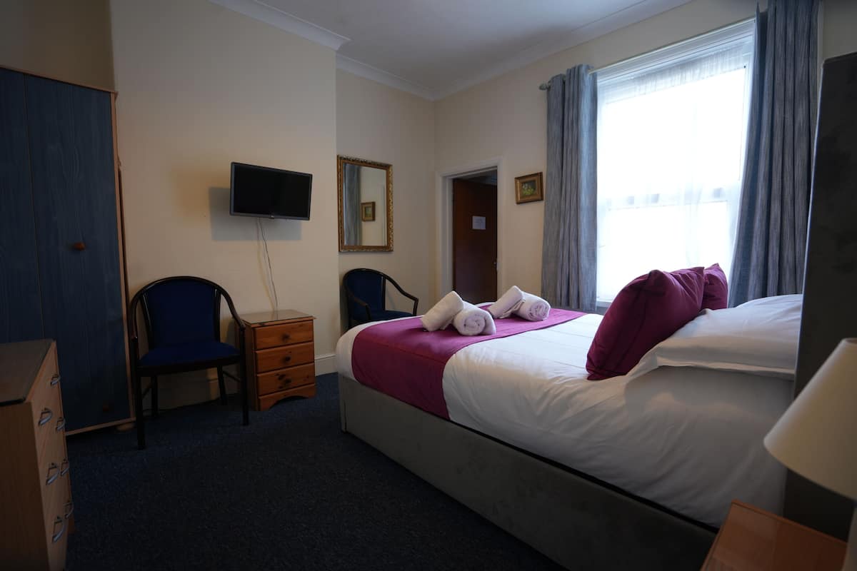 A hotel room with a bed, a desk, a chair, a wardrobe, a television, and a window with curtains.