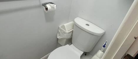 A small, white bathroom with a toilet, a hand dryer, and a trash bin.