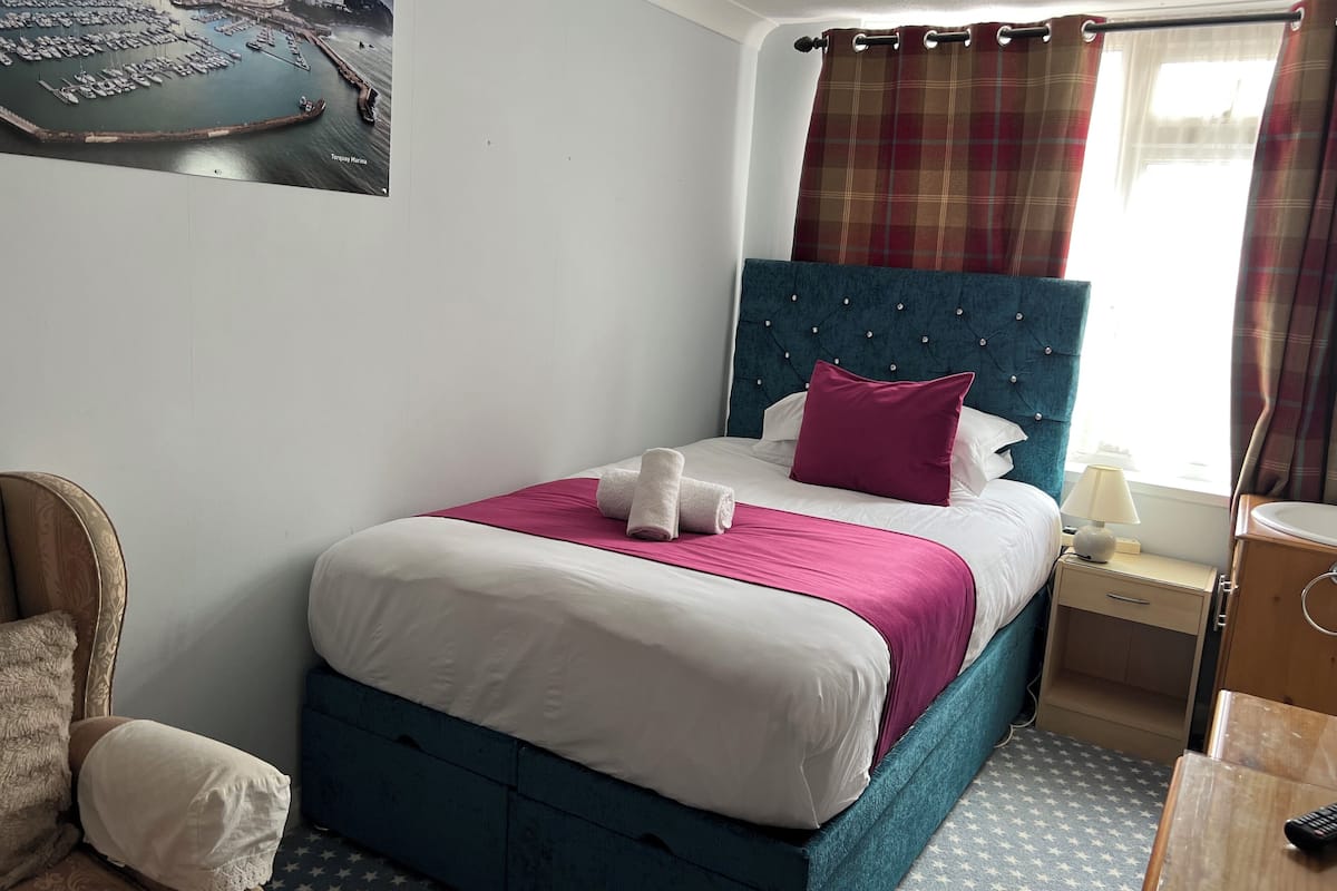A neatly arranged hotel room with a bed, a nightstand, a chair, and a window with curtains.