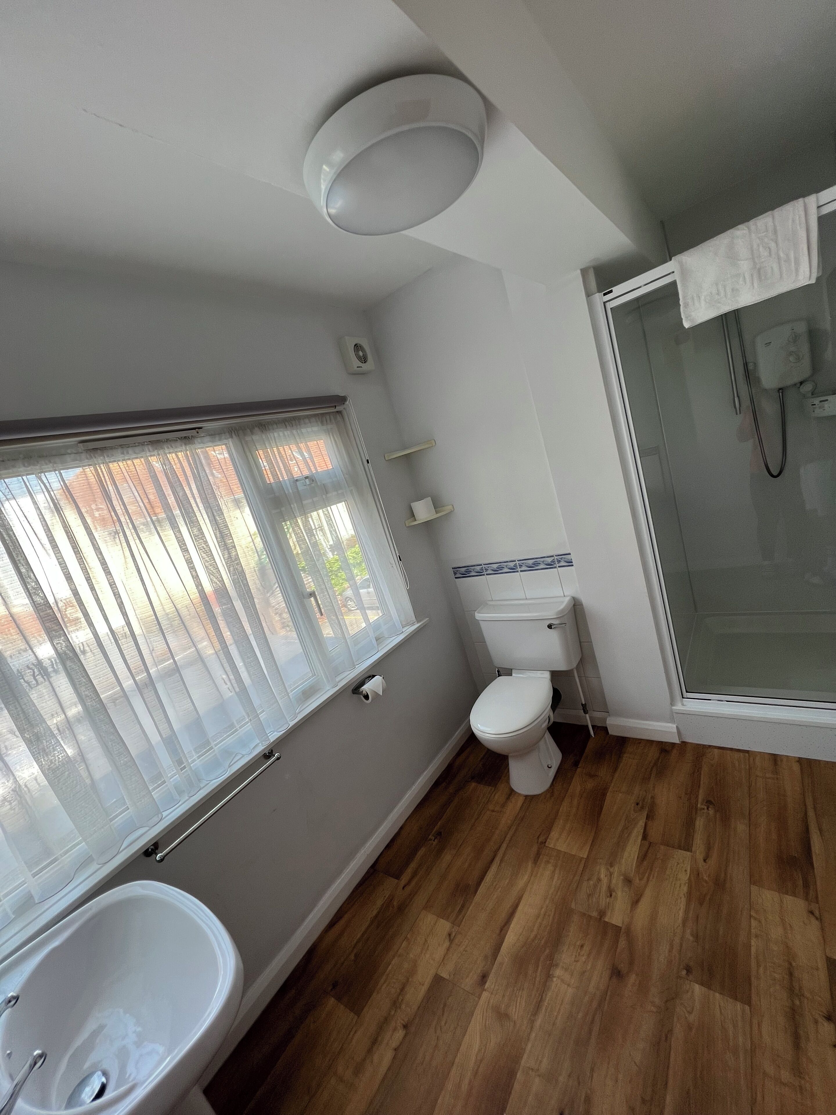 Ein Badezimmer mit Toilette, Bidet und einem Fenster mit durchsichtigen Vorhängen.
