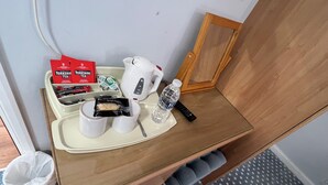 Quarto de hotel com uma penteadeira de madeira, uma bandeja com chá, biscoitos, chaleira e uma garrafa de água, além de um controle remoto.