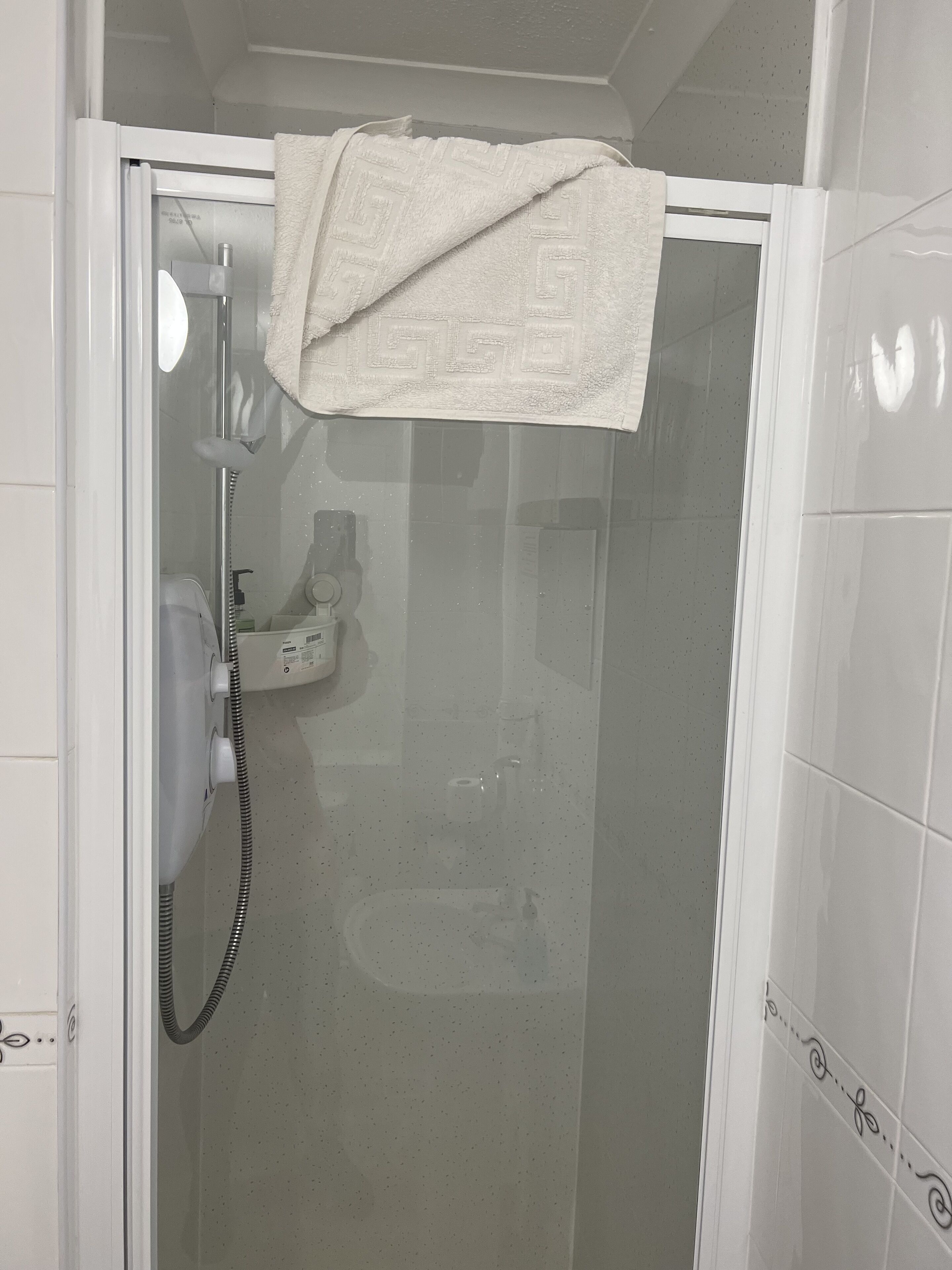 A shower with a glass door, a towel hanging on the door, and a handheld showerhead.