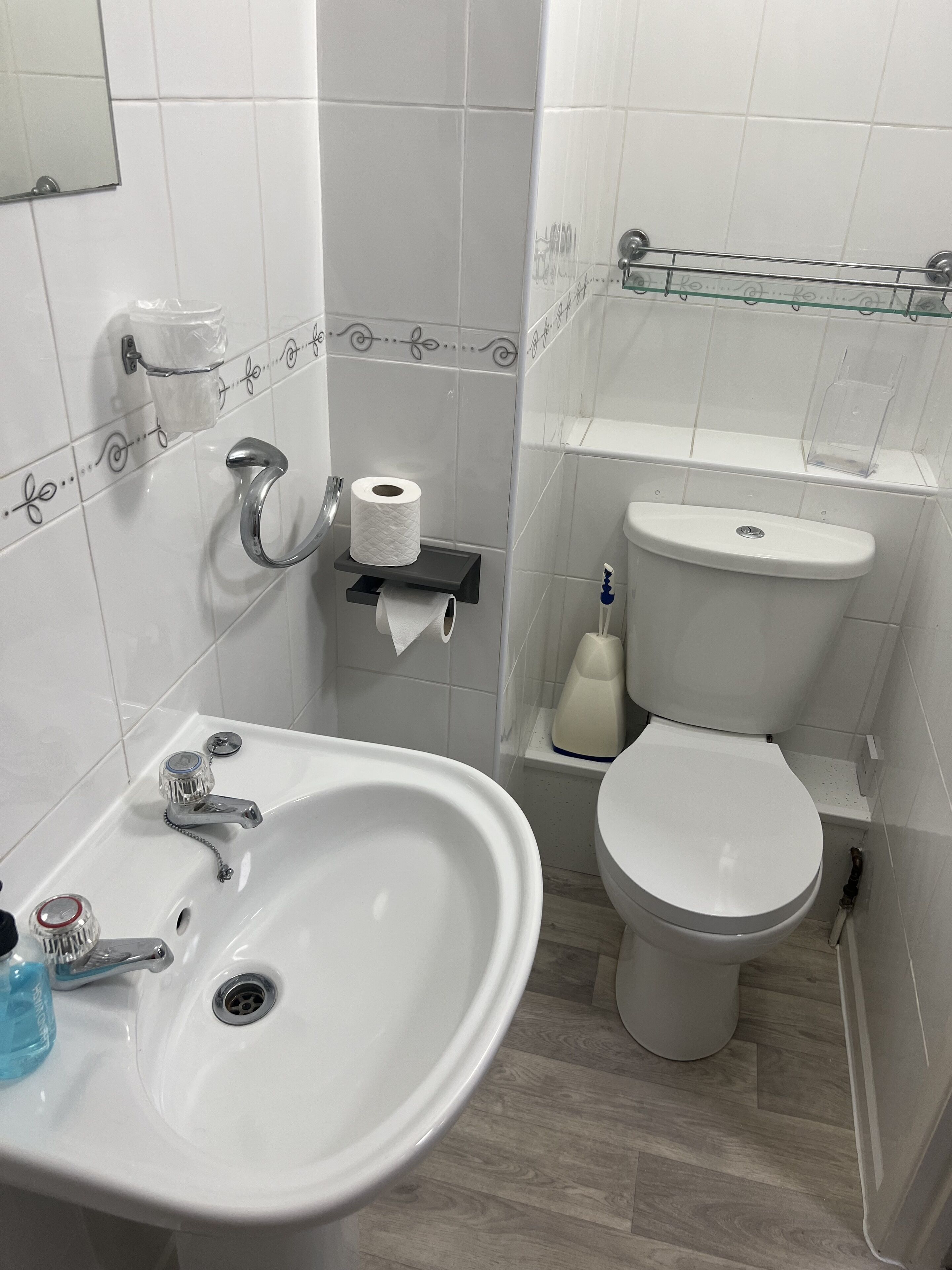 A bathroom with a white sink, toilet, and a glass shelf above the toilet.