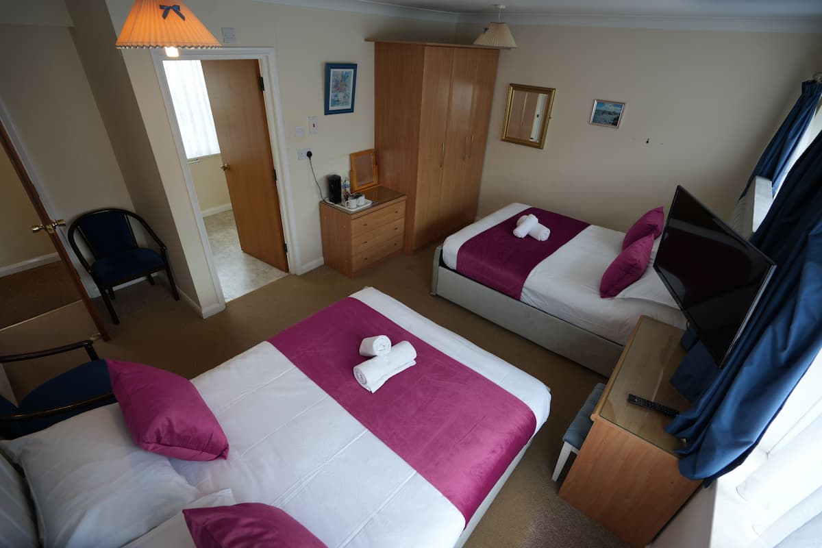 A hotel room with two beds, a desk, a chair, a wardrobe, and a television.