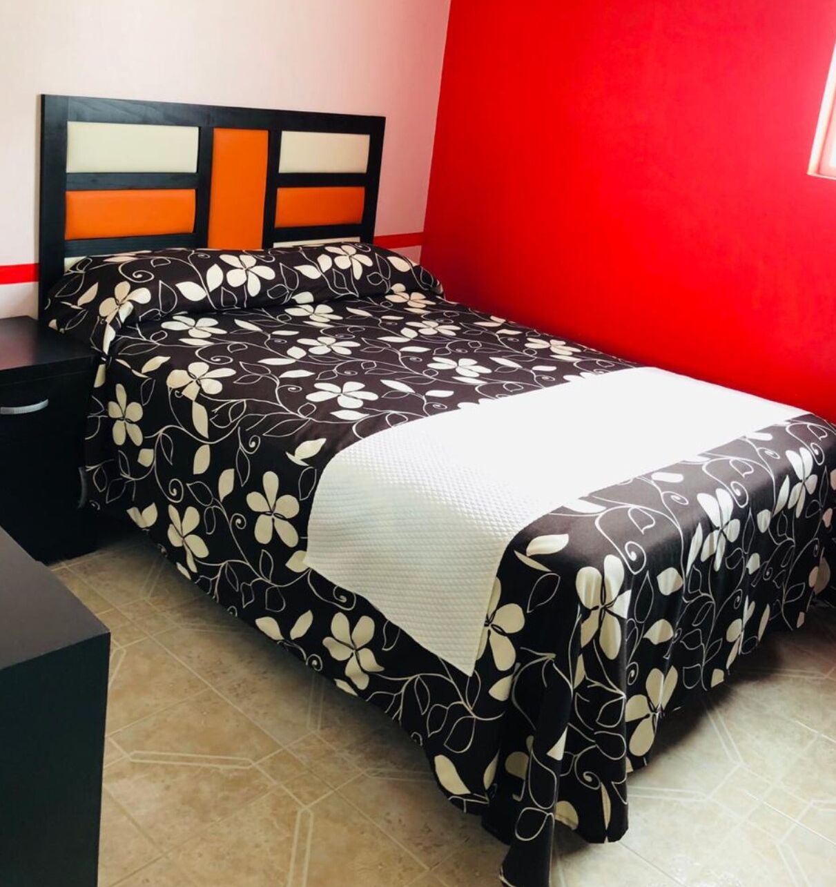A bed with a black and white floral bedspread, a white pillow, and a headboard with orange and white panels.