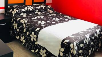 A bed with a black and white floral bedspread, a white pillow, and a headboard with orange and white panels.