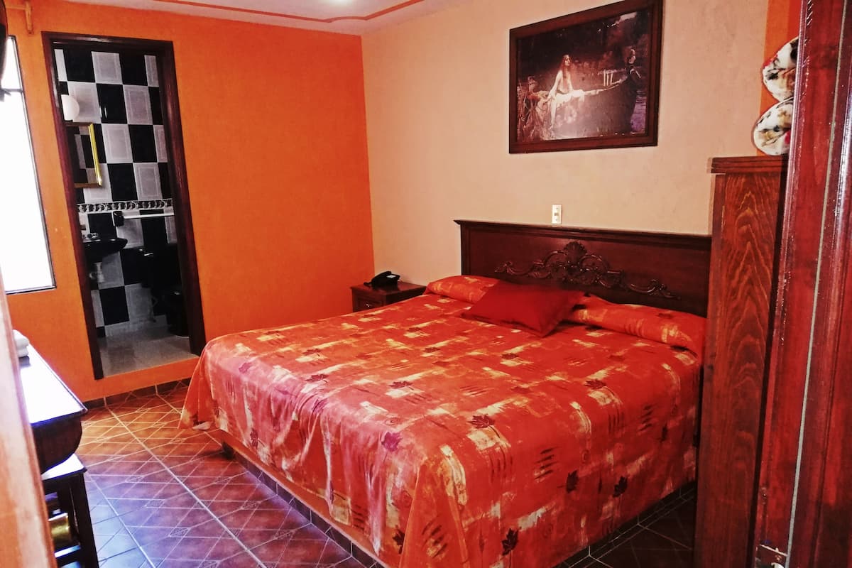 Un dormitorio con una cama grande, cabecera de madera, una mesita de noche, un teléfono y un cuadro en la pared.