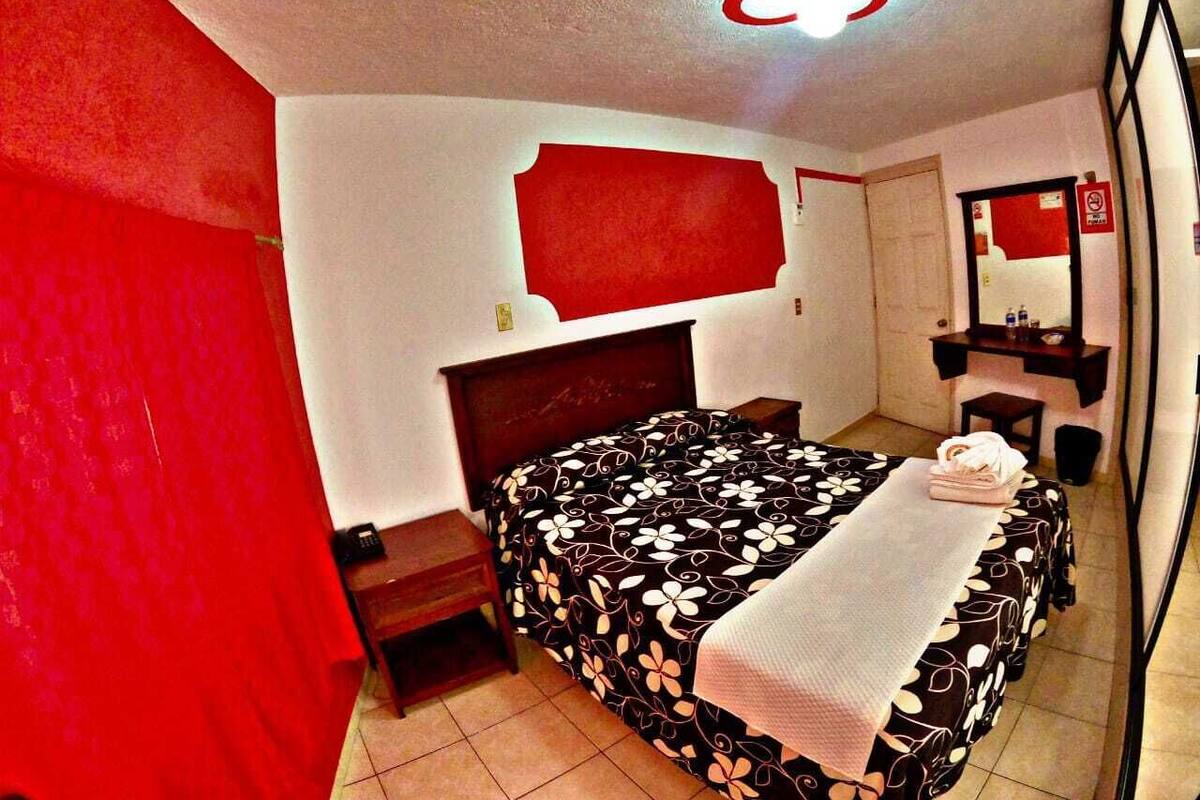 Una habitaci ón de hotel con una cama, una mesita de noche, un espejo y una pared roja.