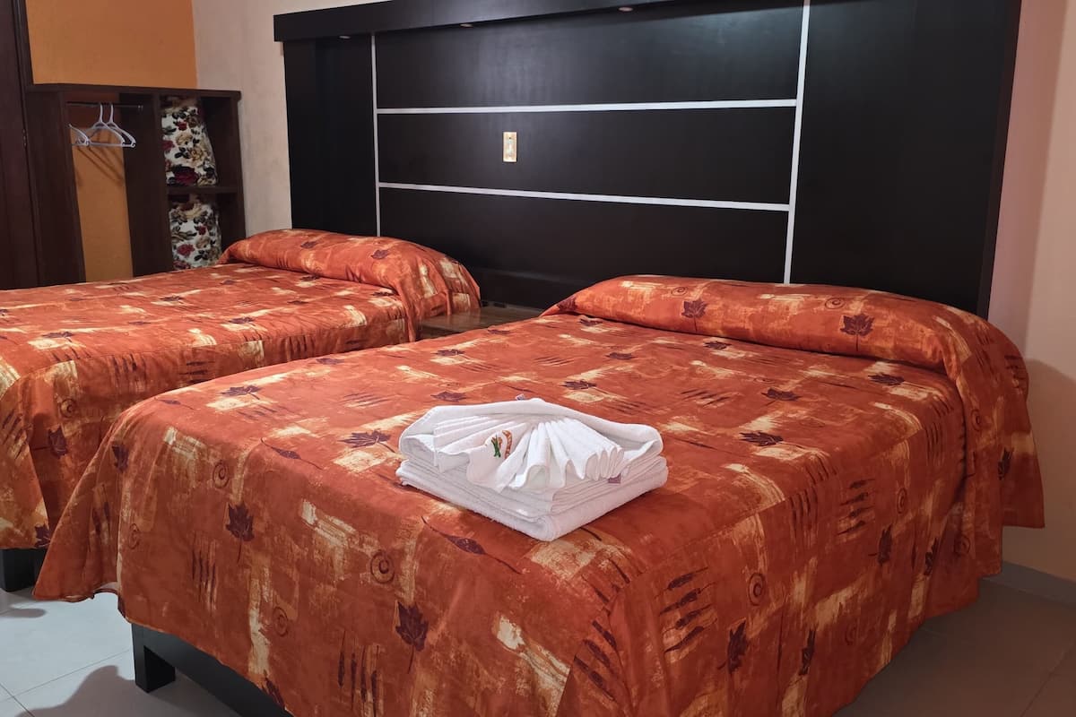 Habitación de hotel con dos camas, cabecera oscura y suelo de baldosas.