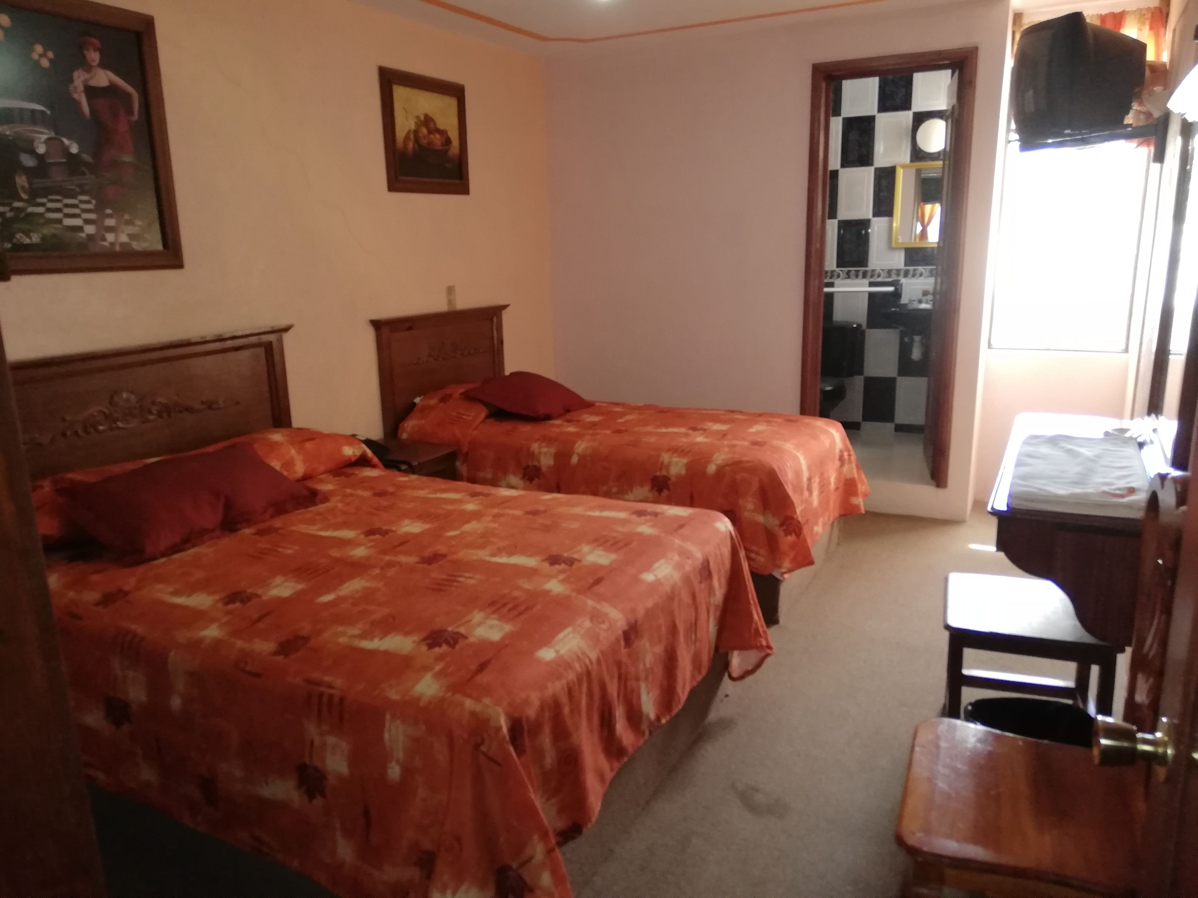 A bedroom with two single beds, a wooden headboard, a small wooden table, and a television mounted on the wall.