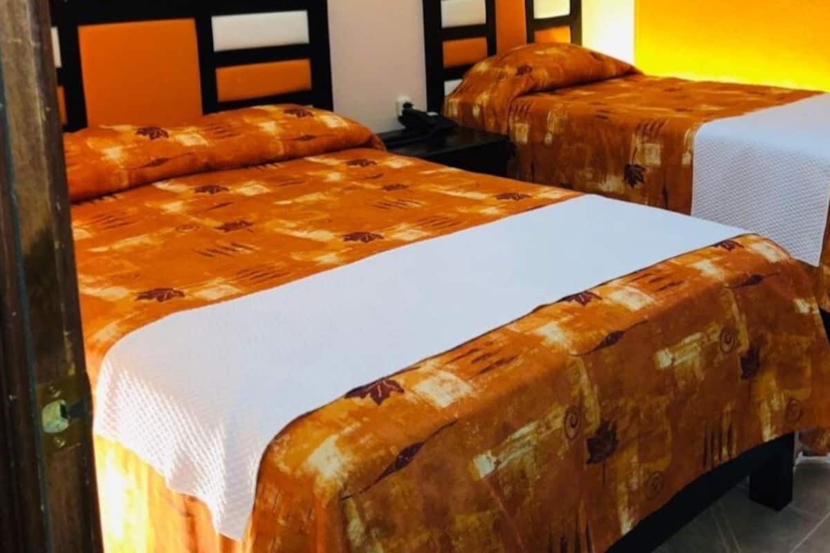 Dos camas individuales con colchas estampadas en una habitación con suelo de baldosas y cabecero de madera.