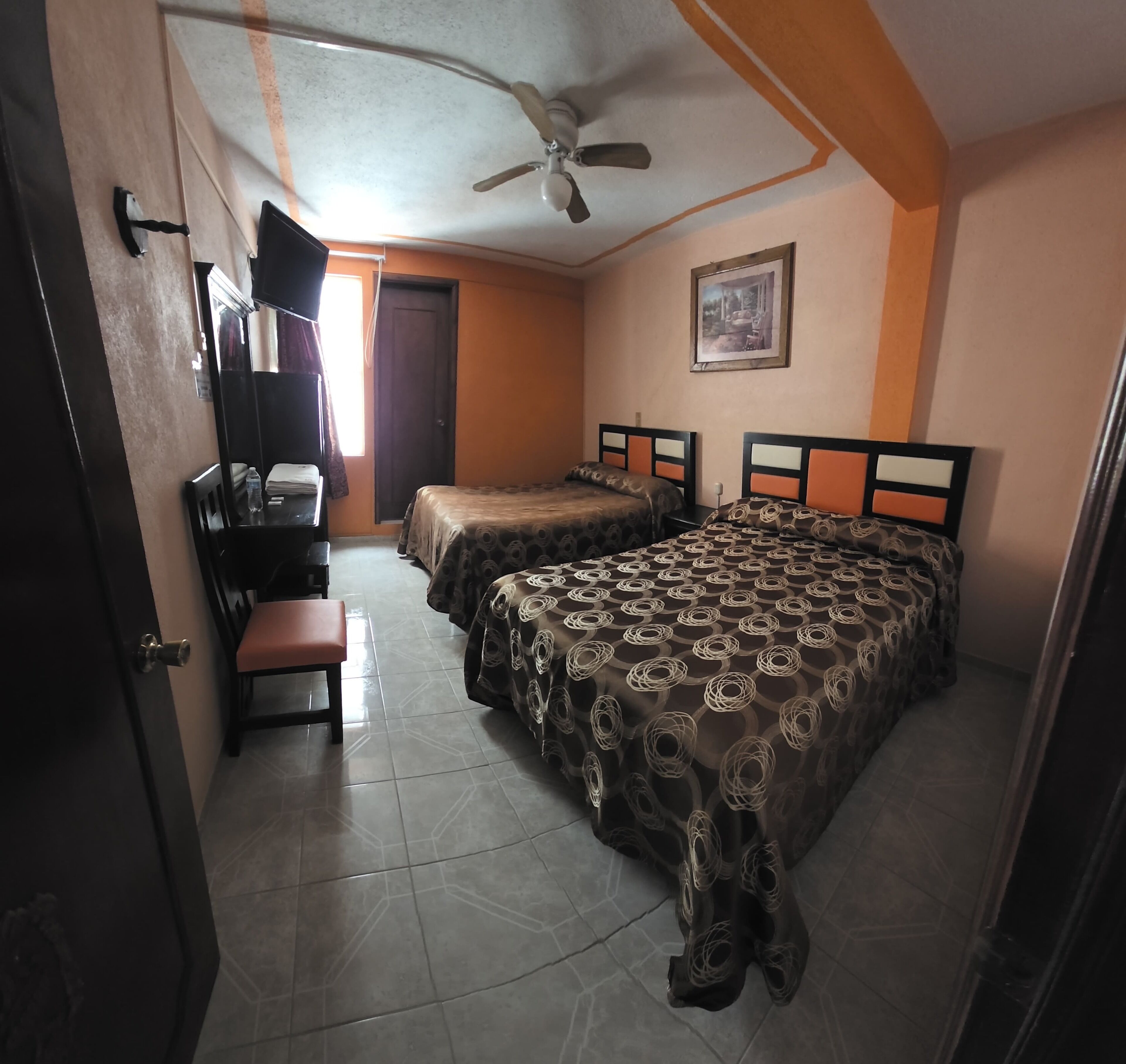 A room with two beds, a desk, a chair, and a ceiling fan.