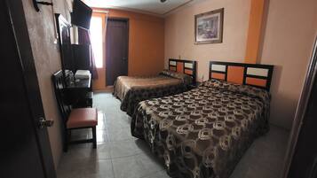 A room with two beds, a desk, a chair, and a ceiling fan.