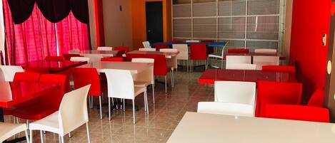 A restaurant with red and white tables and chairs, a tiled floor, and a window with a view.
