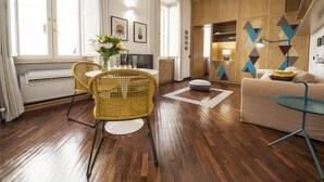 A modern living room with a wooden floor, a yellow wicker chair, a beige sofa, and a small round table. - Rome as you feel - Baccina 95 Forum Apartment (Rome)