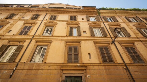A multi-story building with a classic architectural style, featuring evenly spaced windows and shutters, and a prominent entrance with a door. - Rome as you feel - Baccina 95 Forum Apartment (Rome)