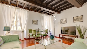A living room with a glass coffee table, green sofas, a TV, and framed pictures on the wall. - Rome as you feel - Panisperna Apartment (Rome)