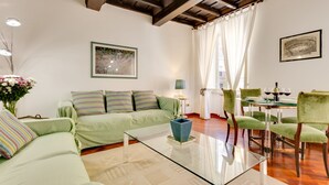 A living room with a glass coffee table, a green sofa, and a dining area with green chairs and a glass table. - Rome as you feel - Panisperna Apartment (Rome)