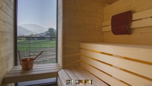 A wooden sauna with a bench, a wooden wall, and a view of a green landscape and mountains through a window. - Chambres D'Hotes La Bicoque (Sarre)