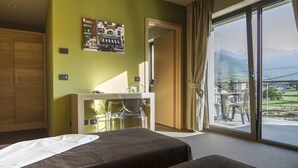A hotel room with two beds, a desk, a chair, and a large sliding glass door leading to a balcony with a view of mountains. - Chambres D'Hotes La Bicoque (Sarre)