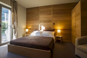 Habitación de hotel moderna con una cama grande, dos mesitas de noche con lámparas, vistas a través de una puerta corrediza y un armario.