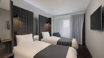 A hotel room with two beds, a TV, a desk, and a large window with curtains.