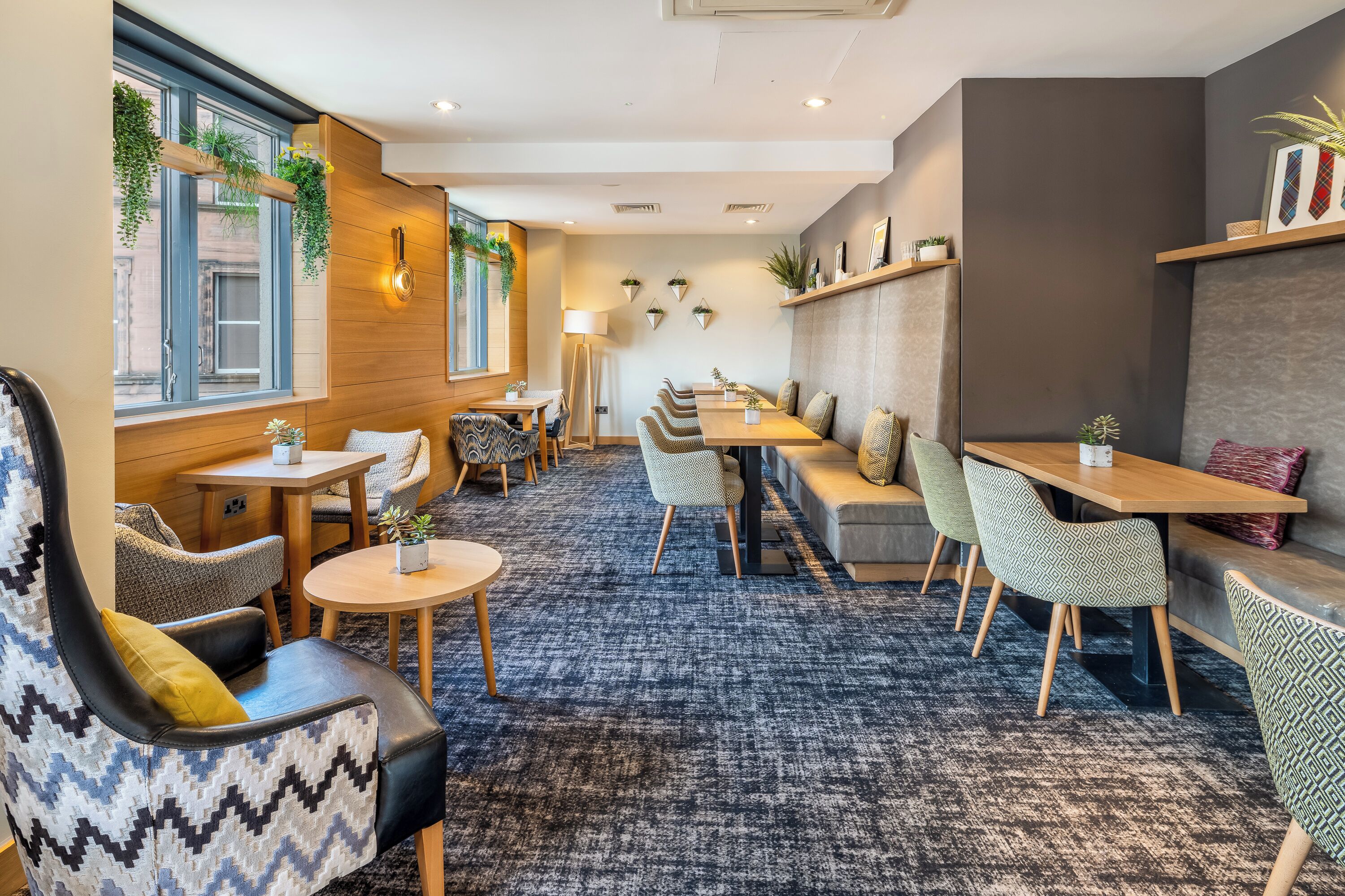 A modern lounge area with seating arrangements, a patterned carpet, and decorative plants.