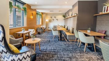 A modern lounge area with seating arrangements, a patterned carpet, and decorative plants.