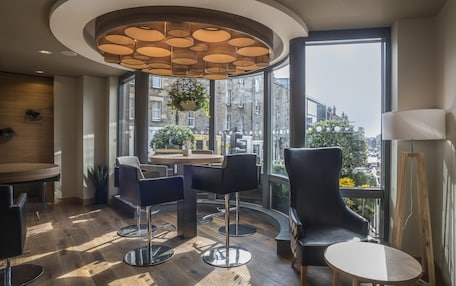 A modern interior with a round table, bar stools, and a large window offering a city view.