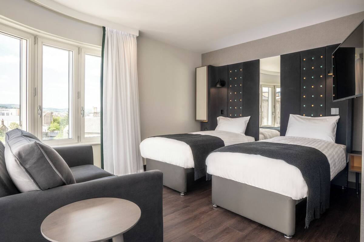 A hotel room with two beds, a sofa, a small table, and a view of the city.