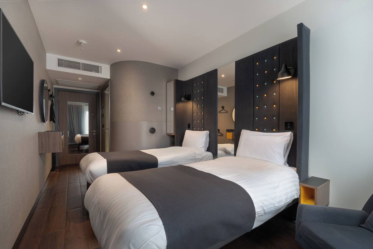A modern hotel room with two beds, a TV, a mirror, and a wardrobe.