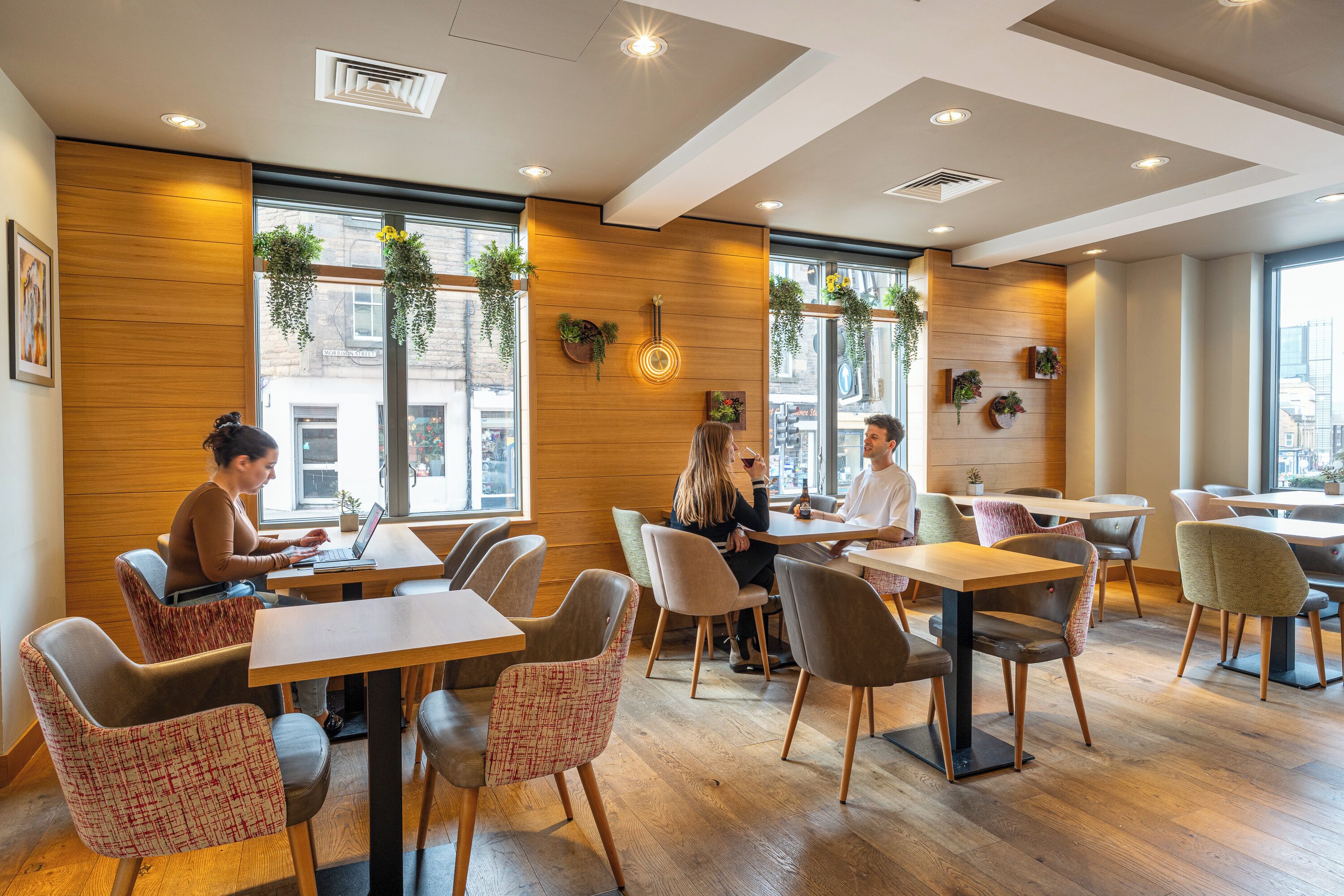 A modern cafe with wooden walls, large windows, and indoor plants.