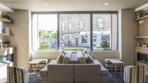 Un salon moderne avec un canapé, deux tables d’appoint et une grande fenêtre donnant sur une rue et des immeubles.