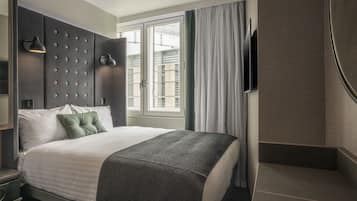 A modern hotel room with a large bed, a flat-screen TV mounted on the wall, and a window with curtains.
