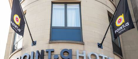 Hotellets facade, hvor 'POINT.A HOTEL' er tydeligt vist. To flag med hotellets logo er synlige.