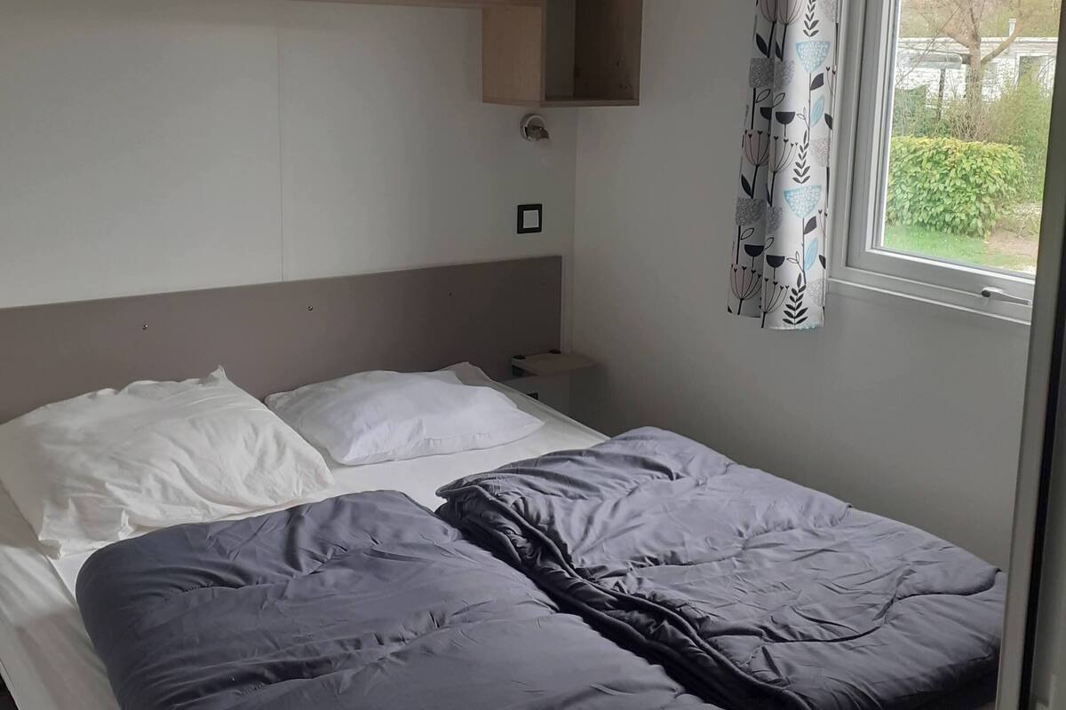 A bedroom with a bed, a headboard, a window with curtains, and built-in shelves.