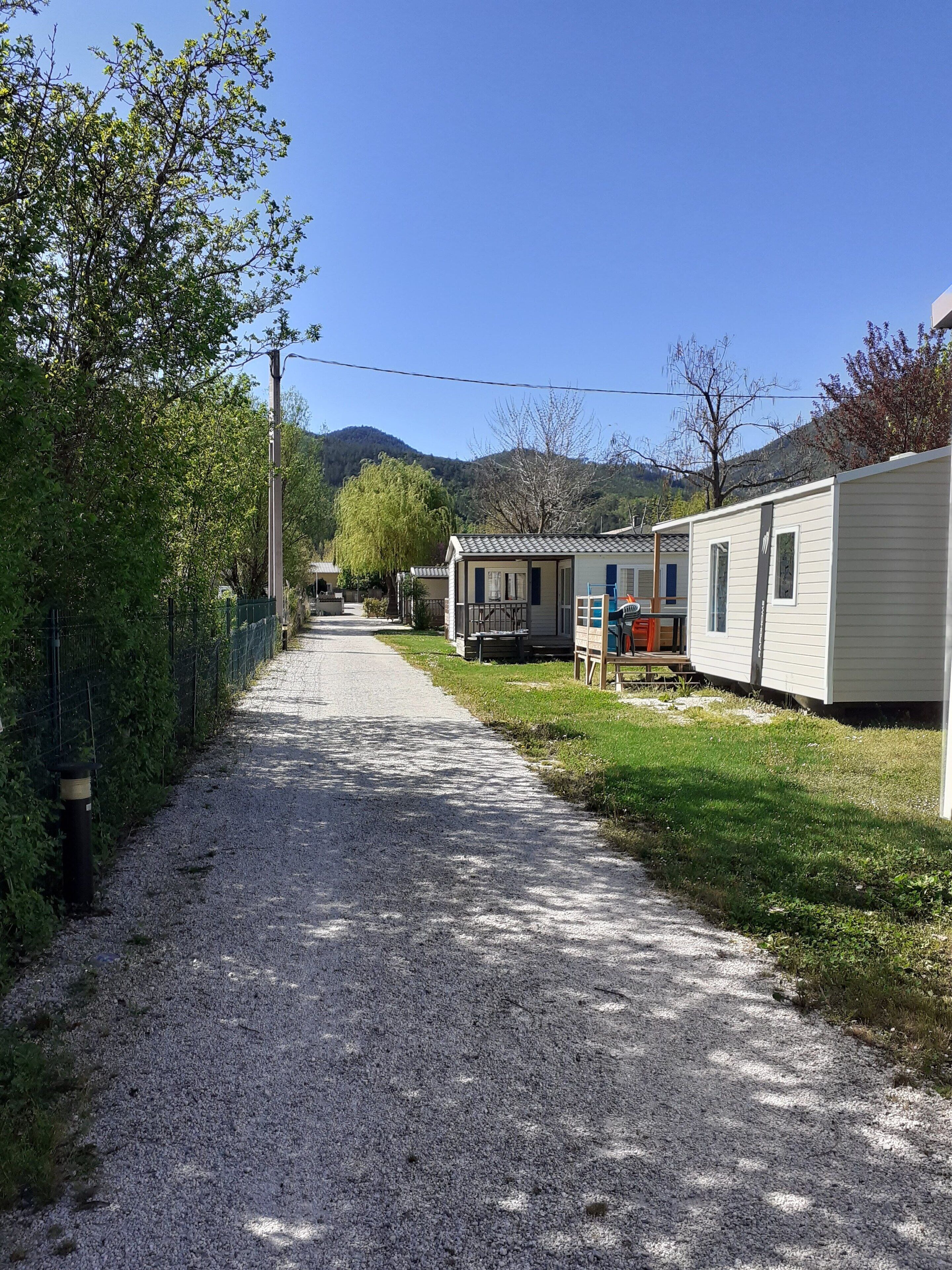 A gravel path leading to mobile homes with a grassy area and trees on one side.