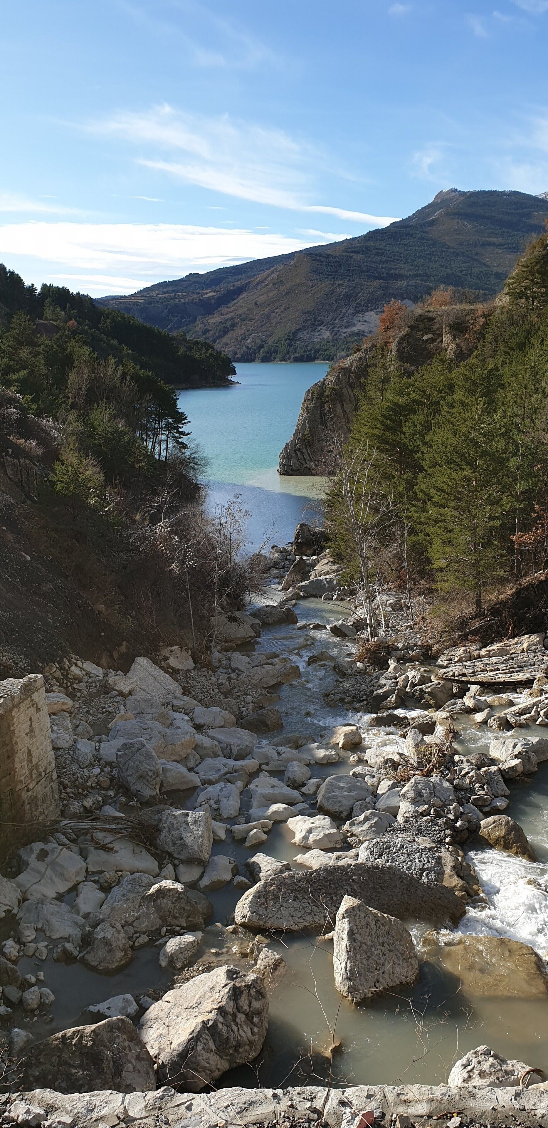 Ein steiniges Flussbett mit freiem Blick auf einen See und umliegende Hügel.